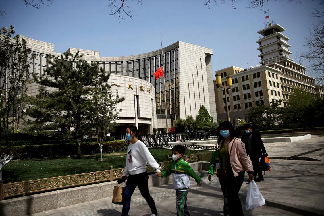 FILE PHOTO: People walk past the headquarters of Chinese central bank People's Bank of China (PBOC), April 4, 2020. REUTERS/Tingshu Wang/File Photo