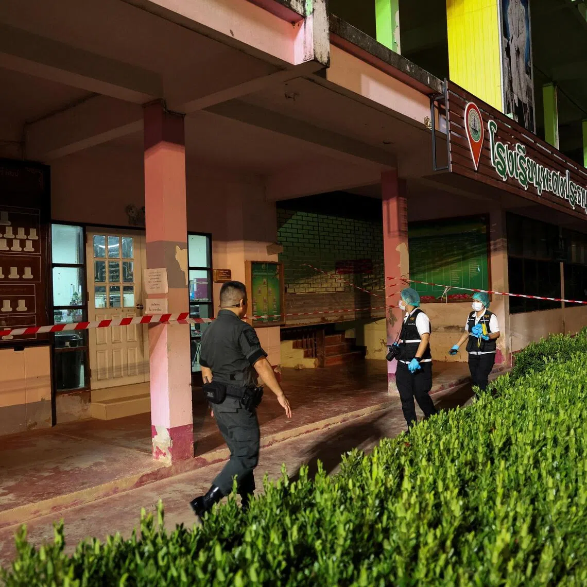 Members of the forensic team and a police officer walk near the building inside Patongprathankiriwat School.