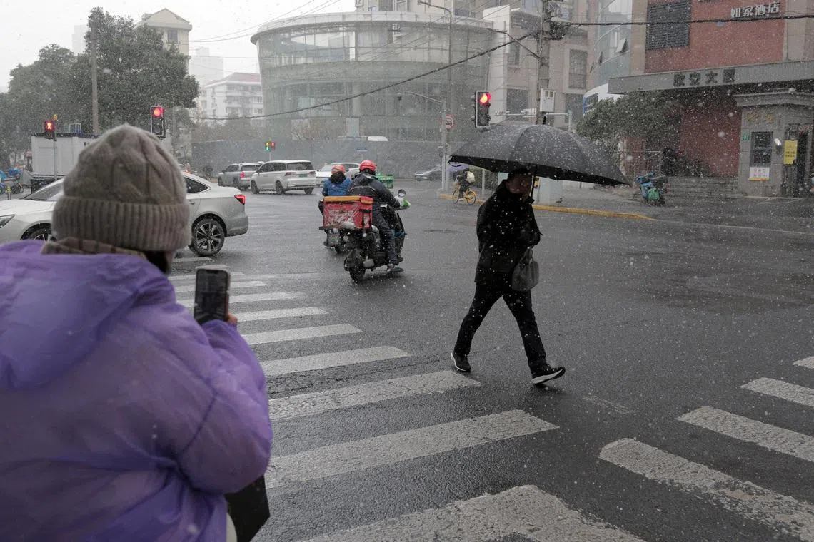 A pedestrian holding an umbrella crosses an intersection amid snowfall in Shanghai, China January 20, 2026. REUTERS/Go Nakamura