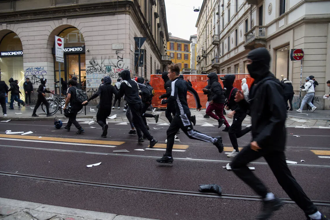 Protesters run along a street strewn with debris during a protest over the state of public services and the rising cost of living in Milan, Italy, on Oct 18.