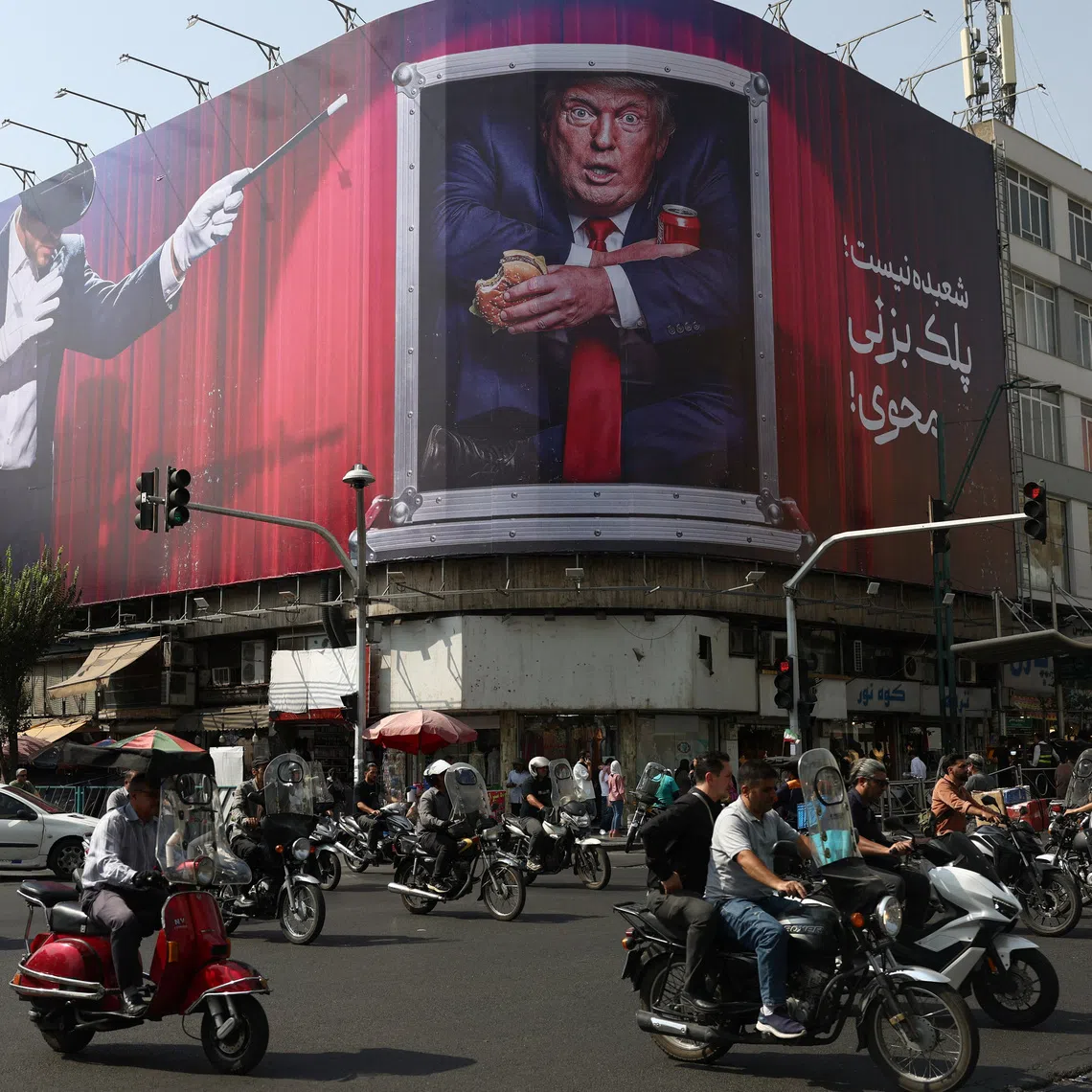 People drive near a billboard depicting US President Donald Trump on a building in Tehran.
