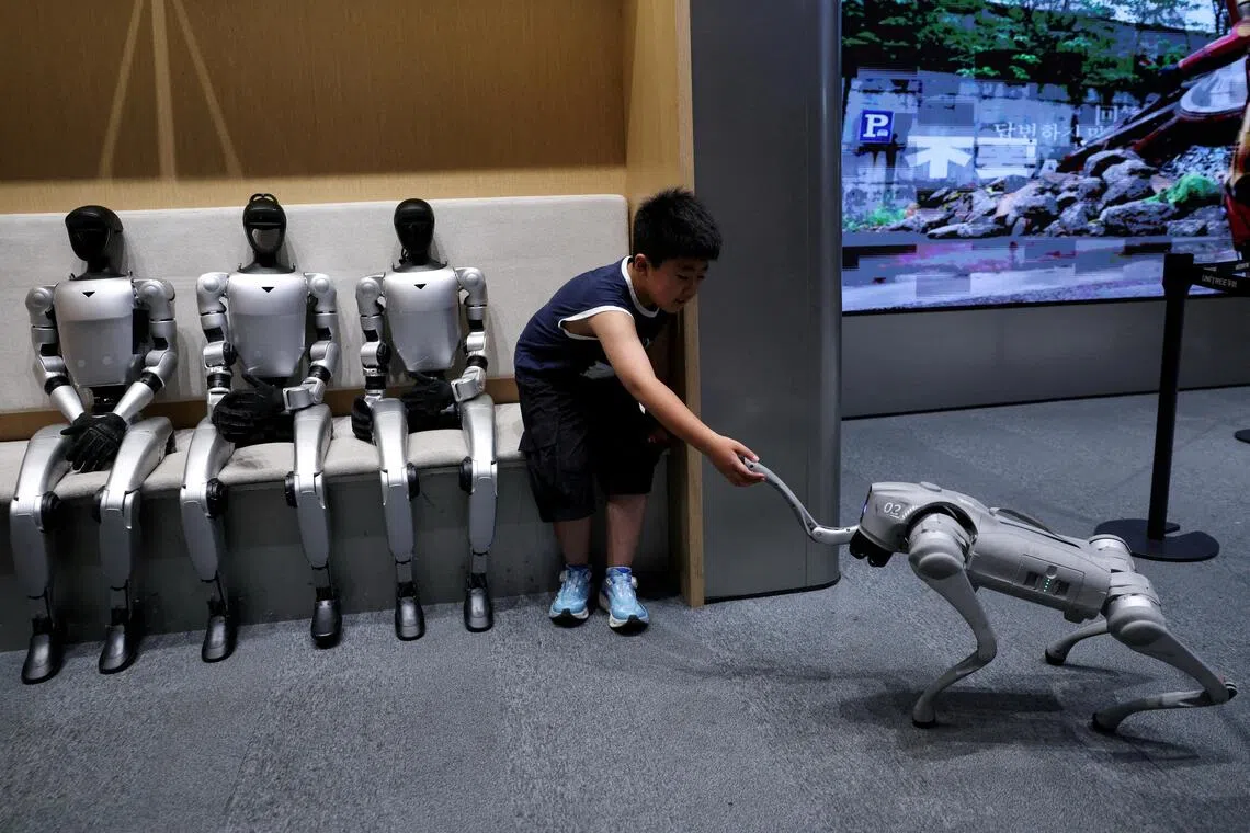 A child sits next to Unitree’s G1 humanoid robots, as he interacts with Unitree GO2 robot.