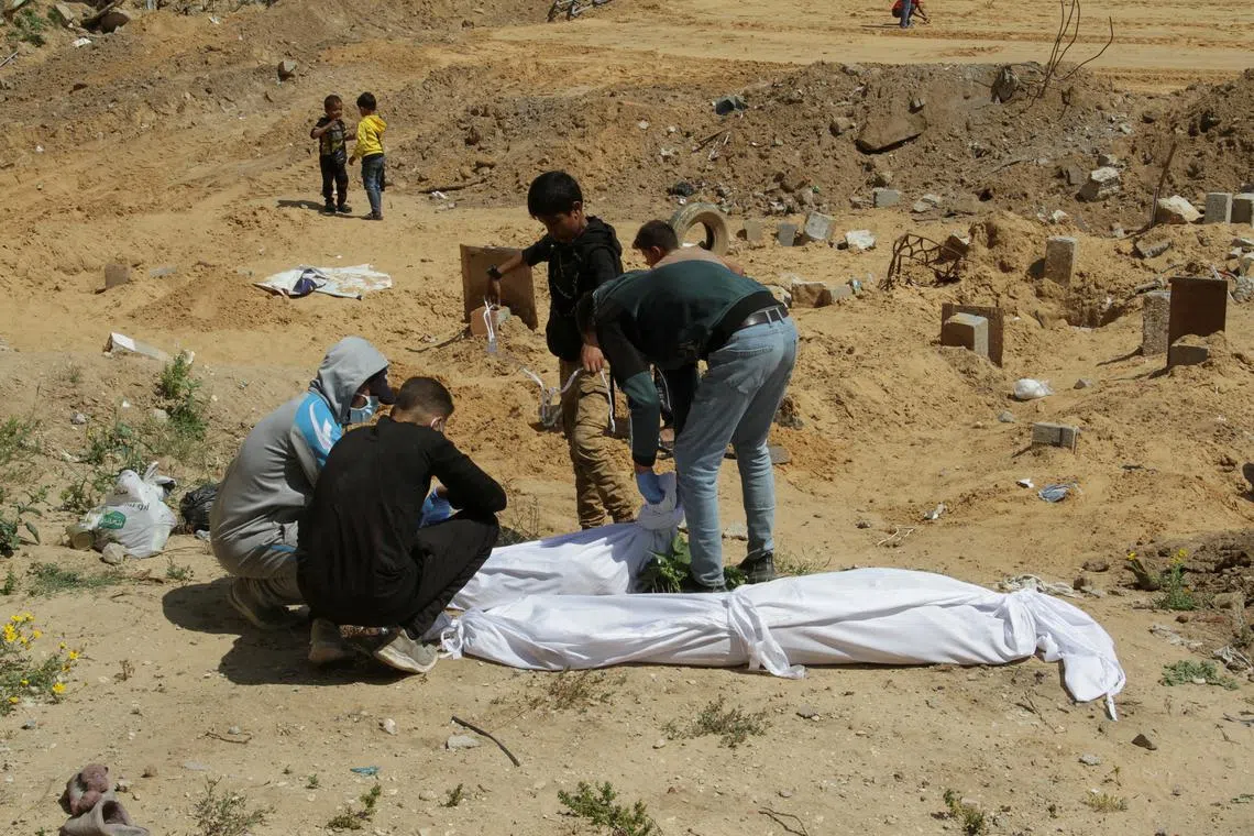 Palestinians cover a body, which was buried in a mass grave, amid the ongoing conflict between Israel and Hamas, in northern Gaza Strip, April 15, 2024. REUTERS/Mahmoud Issa/File Photo