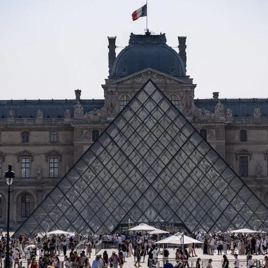 Tourists walking past the Louvre Museum and the Pyramide du Louvre in central Paris.