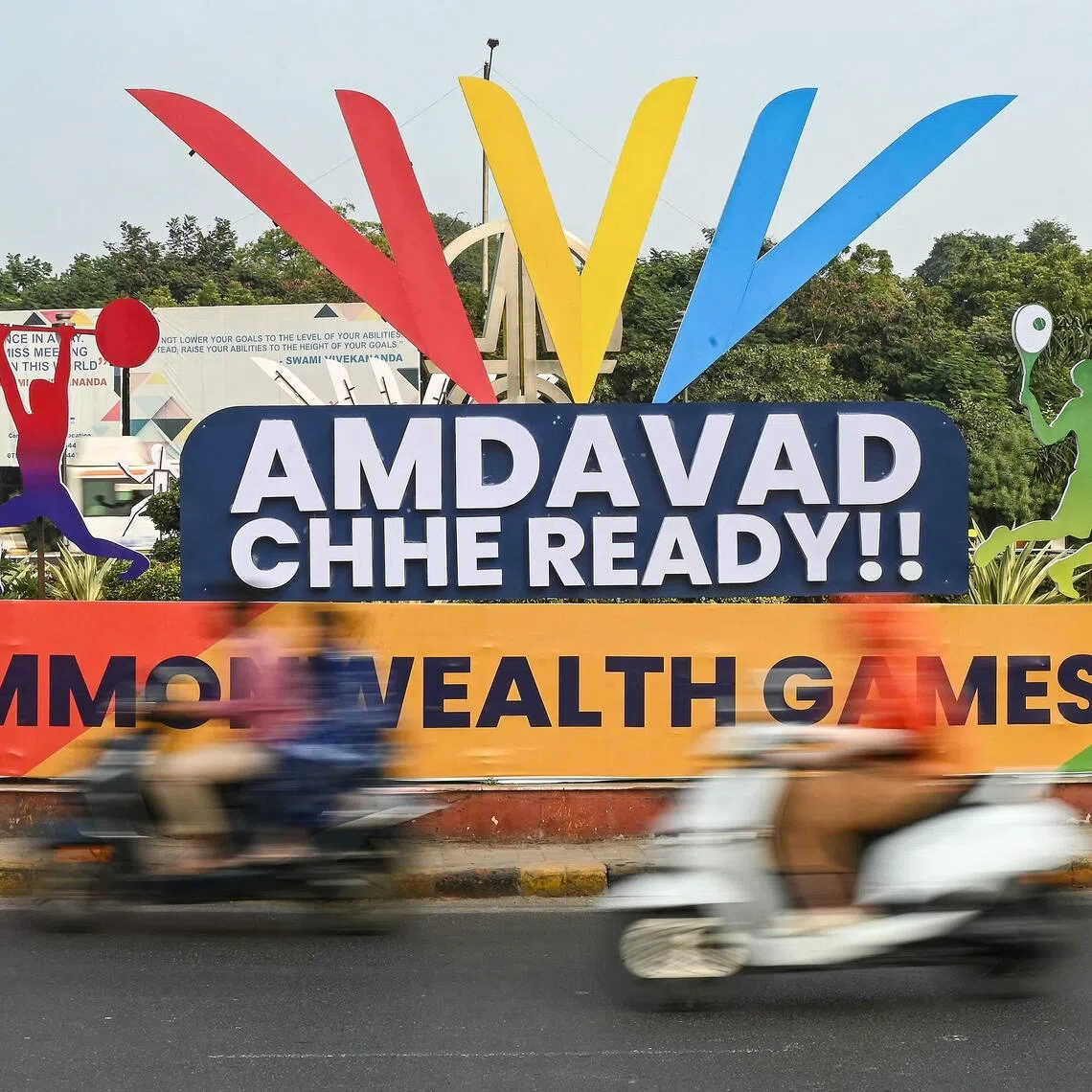 Commuters ride past a signboard cut-out advertising the 2030 Commonwealth Games in Ahmedabad on Nov 29, 2025. 