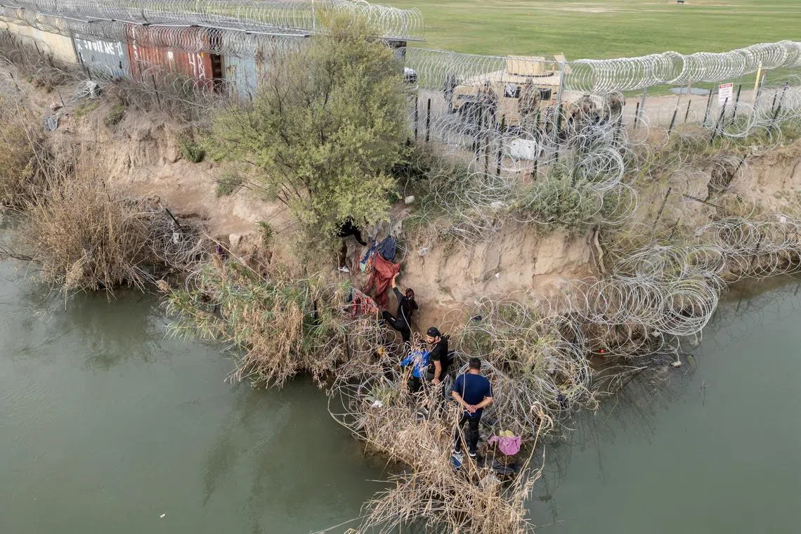 FILE PHOTO: A group of migrants attempt to go through a wire fence on the banks of the Rio Grande river as members of U.S. National Guards stand guard on the other side of the fence in Eagle Pass, Texas, U.S., February 27, 2024. REUTERS/Go Nakamura/File Photo
