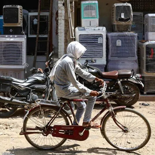 A man with his face covered to beat the heat riding past air coolers displayed outside a shop on a hot summer day in Varanasi, India.