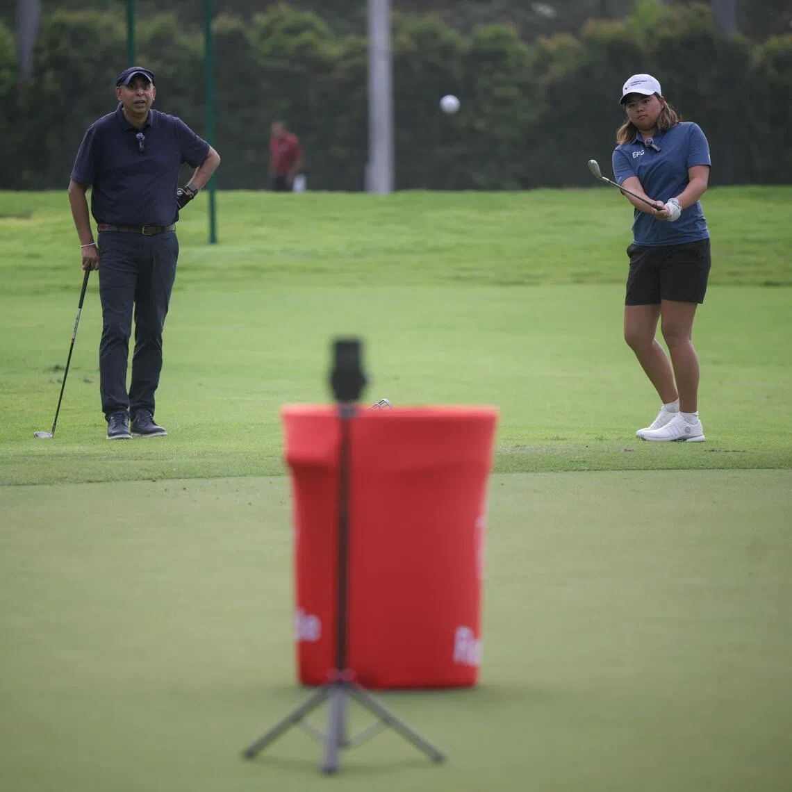 The Straits Times Assistant Sports Editor Rohit Brijnath (left) watches as Singaporean professional golfer Shannon Tan chips a ball during a chipping challenge at Sentosa Golf Club on Feb 21, 2026.