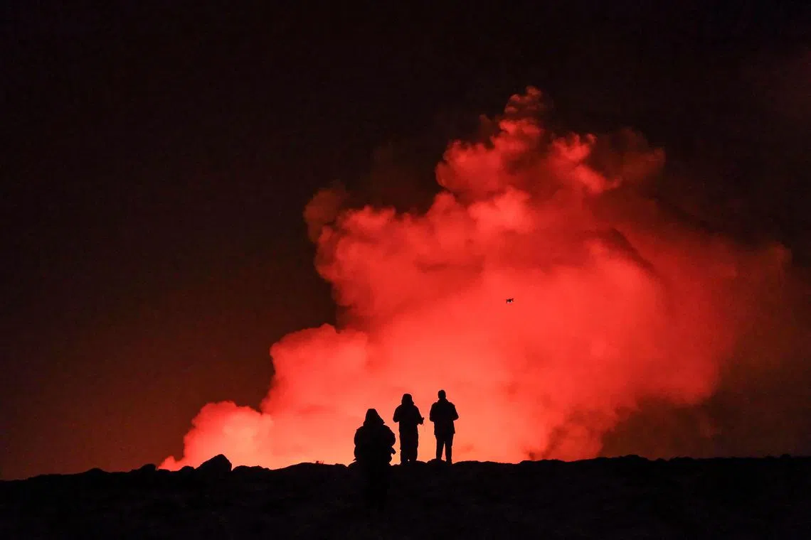 TOPSHOT - A group of people observem molten lava and billowing smoke pouring out of a fissure during a volcanic eruption near Grindavik, western Iceland on February 8, 2023. A volcanic eruption started on the Reykjanes peninsula in southwestern Iceland on Thursday, the third to hit the area since December, authorities said. (Photo by Kristinn Magnusson / AFP) / Iceland OUT
