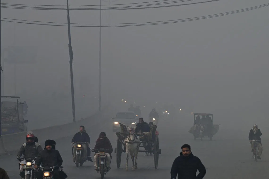 Commuters make their way along a road amid foggy weather in Lahore on December 21, 2022. (Photo by Arif ALI / AFP)