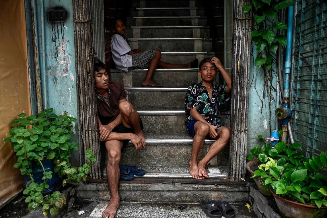 TOPSHOT - People take shelter from the rain on a building staircase in Yangon on August 19, 2025. (Photo by Sai Aung MAIN / AFP)