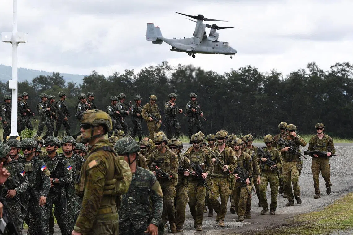 Philippine and Australian soldiers march in formation, while a US V-22 Osprey hovers above during a military exercise.
