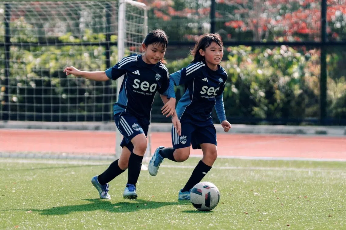 two young lion city sailors girls academy players run with the ball during a youth football game in Singapore