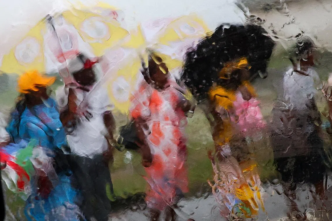People using umbrellas to shelter from the rain as they wait on a street for Pope Leo XIV to pass by, on the day of the pope's visit to the Bata prison, in Bata, Equatorial Guinea, April 22.