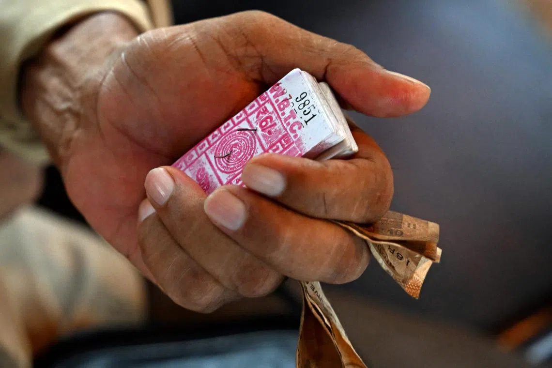 In this photo taken on September 8, 2024, a conductor holds a bunch of tickets, as passengers commute in a tram in Kolkata. Introduced in the sprawling eastern city in 1873 during the early days of the imperial British Raj, trams in Kolkata were initially horse-drawn, then steam-driven. Electric-powered trams took to the streets in 1900. The single-storey trams -- painted in uniform stripes of bright blue and white, with a sunshine yellow top -- trundle at best at around 20 kilometres (12 miles) per hour, if not snarled in traffic blocking its route. (Photo by Dibyangshu SARKAR / AFP) / To go with “Asia’s oldest operating trams see slow death in India” FOCUS