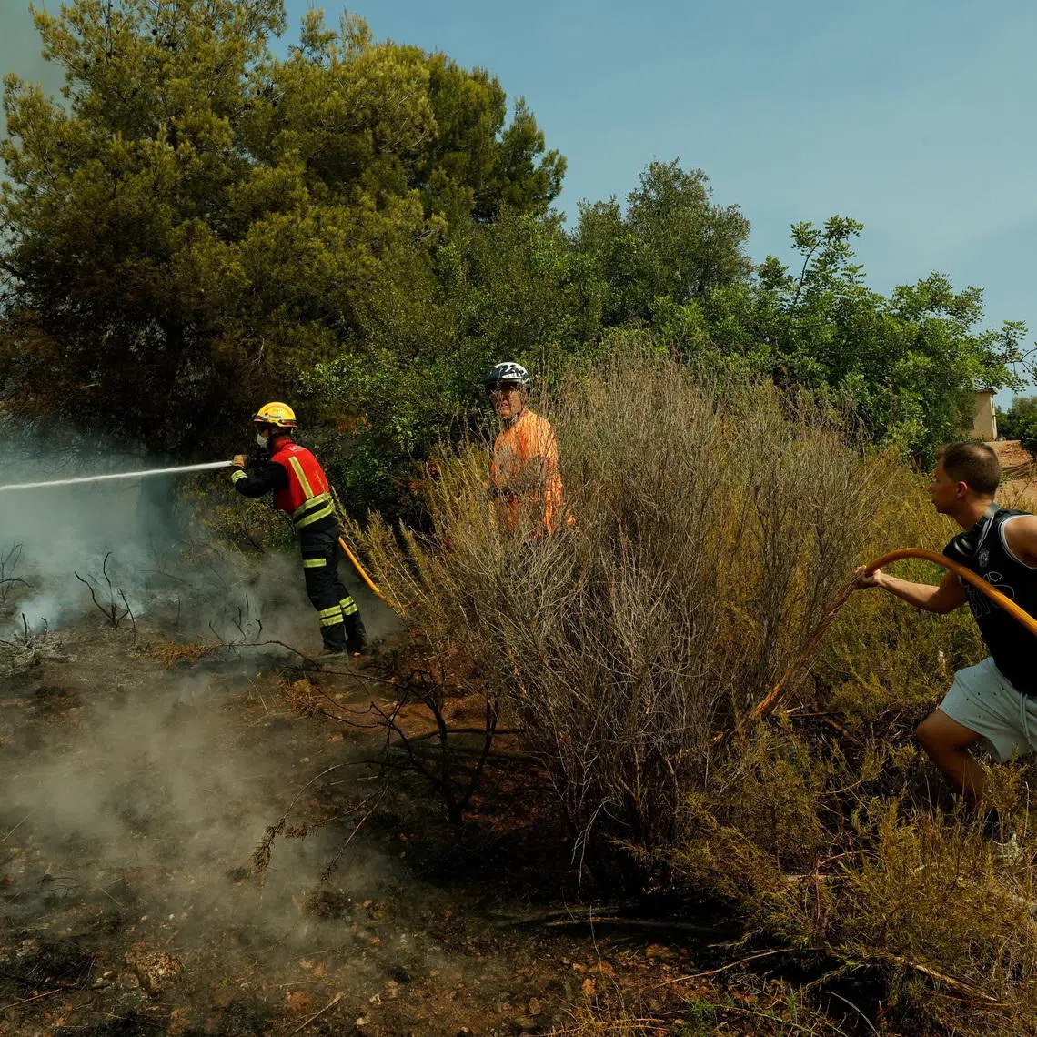 A firefighter uses a hose to extinguish flames during a wildfire in Betxi in Spain.