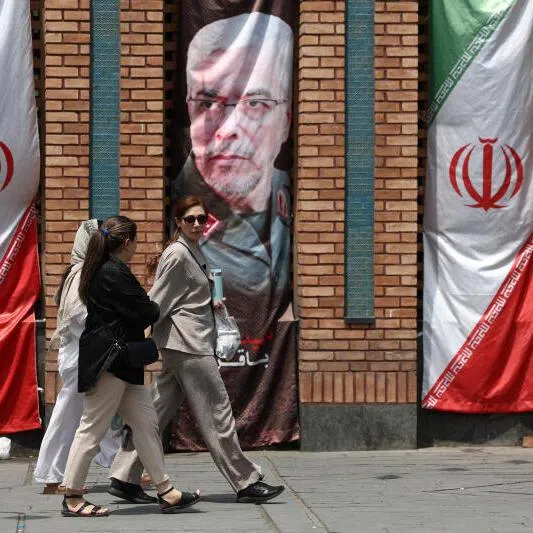 Iranian women walk past a banner with a picture of the former Chief of Staff of the Iranian Armed Forces, Mohammad Bagheri, in Tehran, on July 20, 2026.