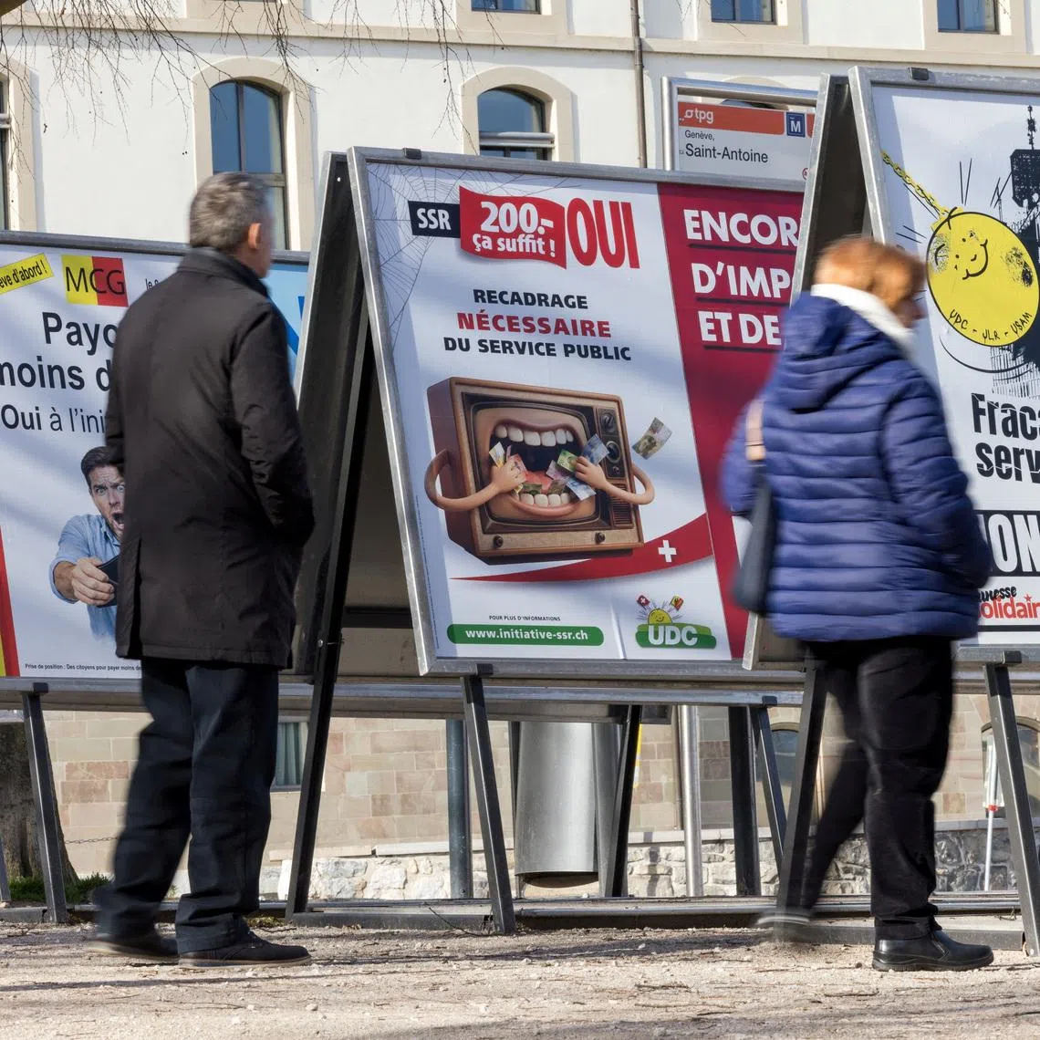 FILE PHOTO: People stand next to posters about funding cuts to the SRG SSR (Swiss Broadcasting Corporation), ahead of the upcoming Swiss national referendum on March 8, in Geneva, Switzerland, February 15, 2026. REUTERS/Pierre Albouy/File Photo