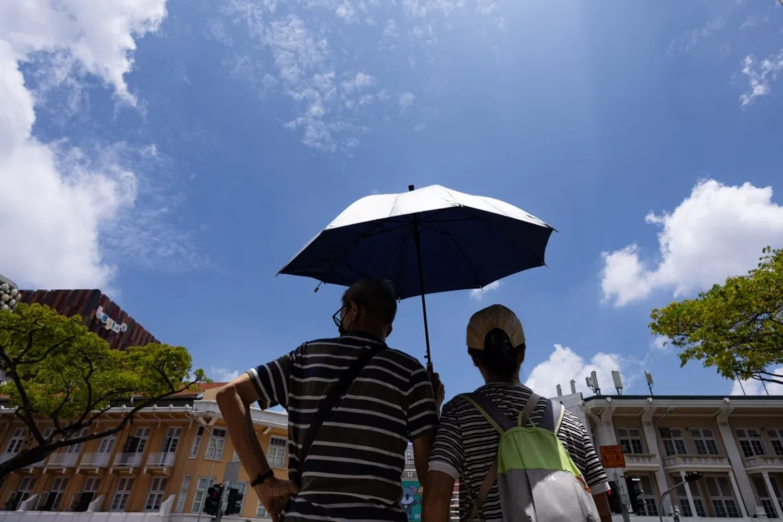Two people in Singapore shielding themselves from the sun with an umbrella
