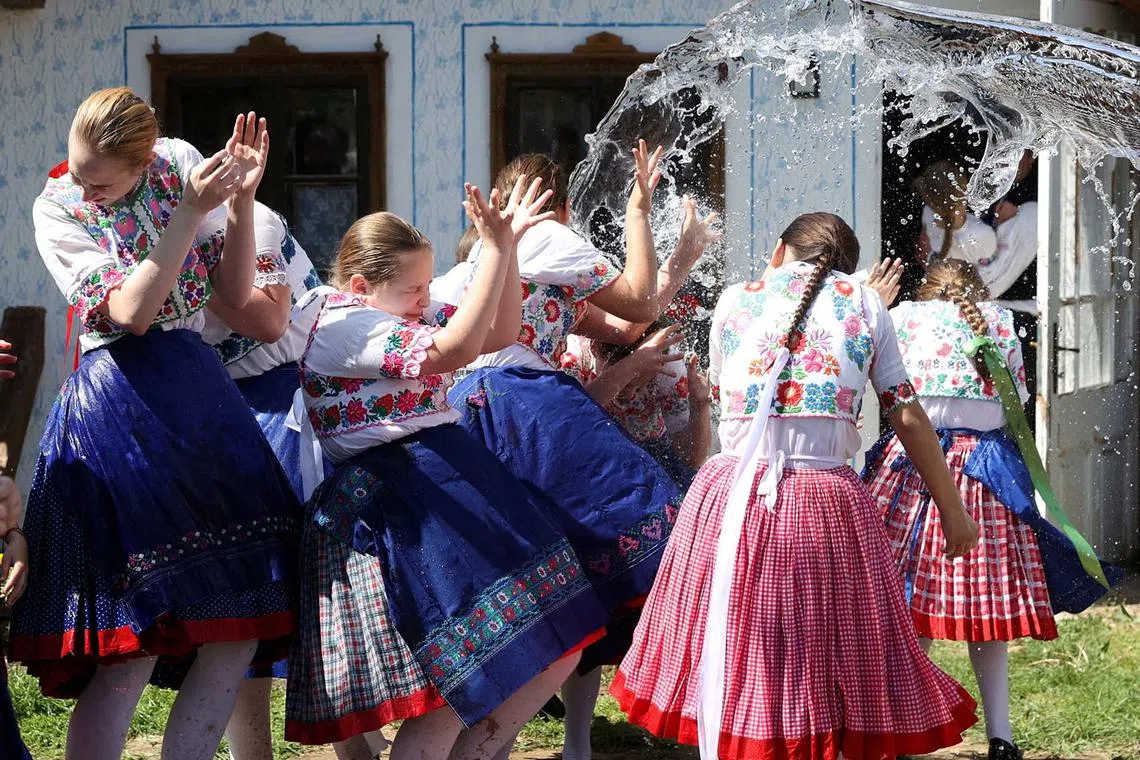 Young girls dressed in traditional clothes reacting to water thrown at them during a traditional Easter celebration in Csomor, Hungary, April 21, 2025. 