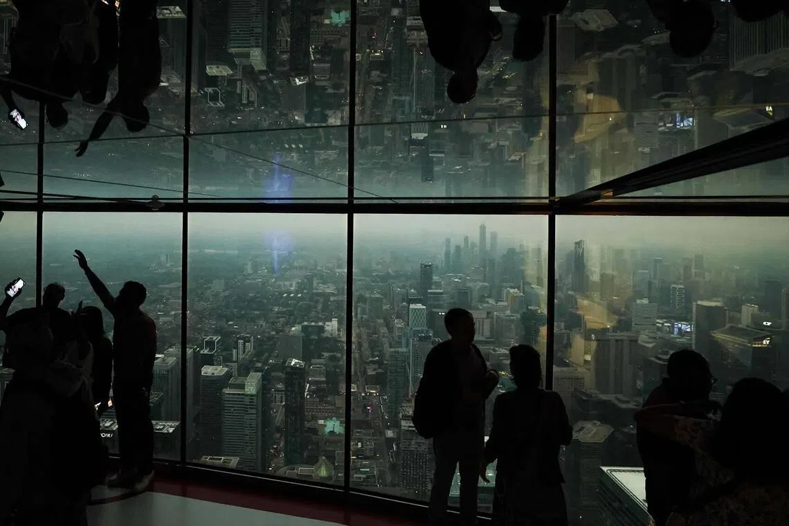 TOPSHOT - People look out from the CN Tower as smoke from wildfires in northern Ontario blankets the city, causing poor air quality, in Toronto, Ontario, Canada, on July 15, 2026. Toronto had the worst air quality of any major city in the world on Wednesday, the Swiss firm IQAir said, as Canadian authorities urged people to stay indoors. Toronto edged out New Delhi and the Democratic Republic of Congo's capital Kinshasa as wildfire smoke turned the skies a hazy yellowish-grey in Canada's largest city. (Photo by Cole BURSTON / AFP)