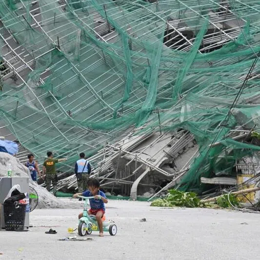 A child riding a tricycle next to a collapsed building in Angeles City, north of Manila, where at least 12 people were believed to be buried.