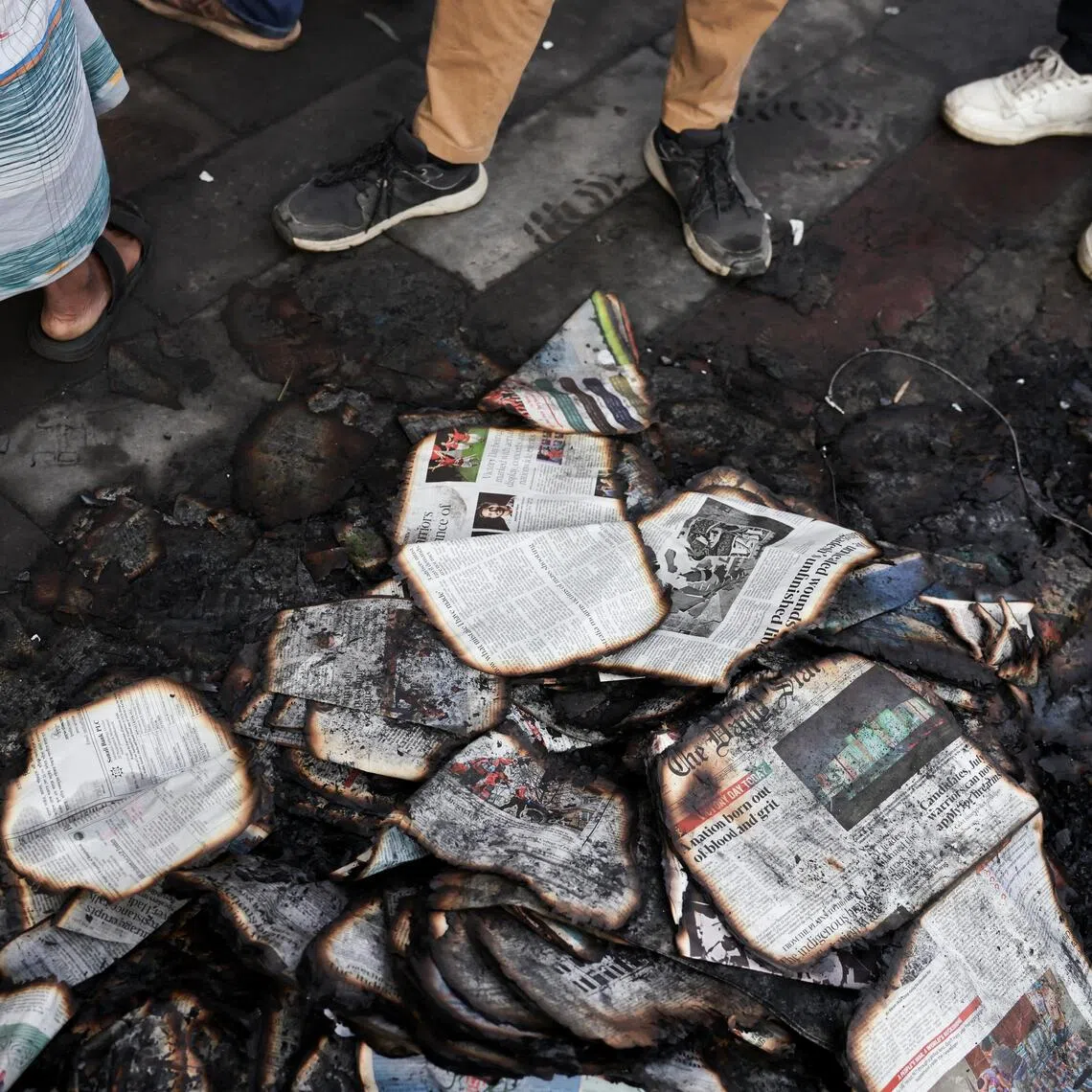 People stand next to burnt newspapers in front of the Daily Star building, following the death of student leader Sharif Osman Hadi, in Dhaka, Bangladesh, on Dec 19, 2025.