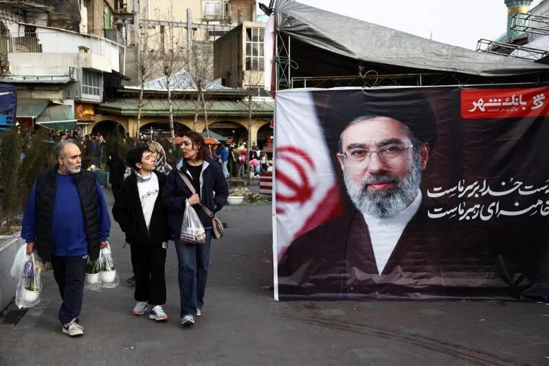People walk next to a banner with a picture of Iranian Supreme Leader, Mojtaba Khamenei, at Tajrish Bazaar, ahead of Nowruz, the Iranian New Year, in Tehran, Iran.