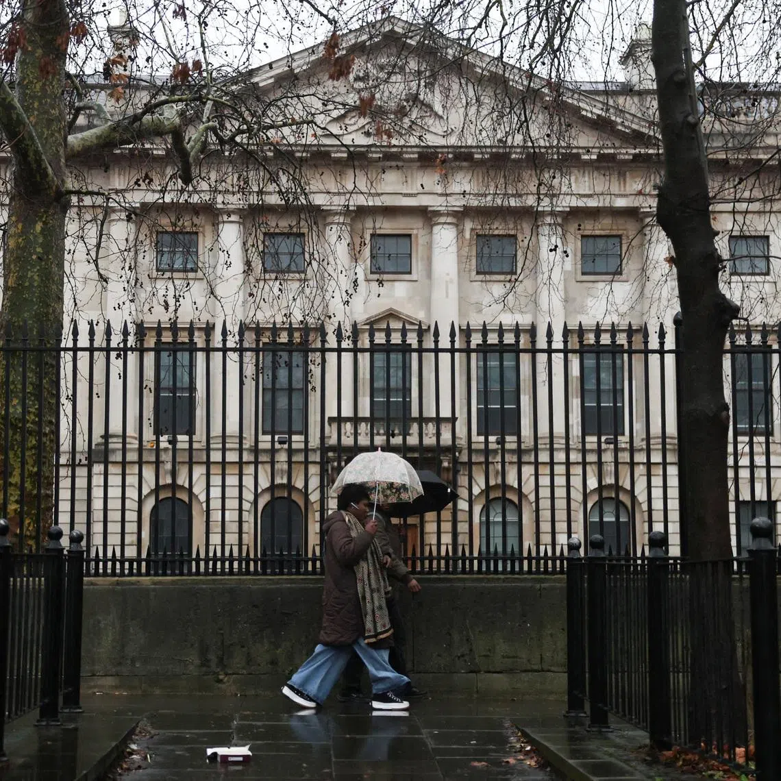 People shelter under umbrellas as they walk past the Royal Mint Court, the proposed site of the new Chinese embassy, in London, Britain, January 13, 2026. REUTERS/Hiba Kola