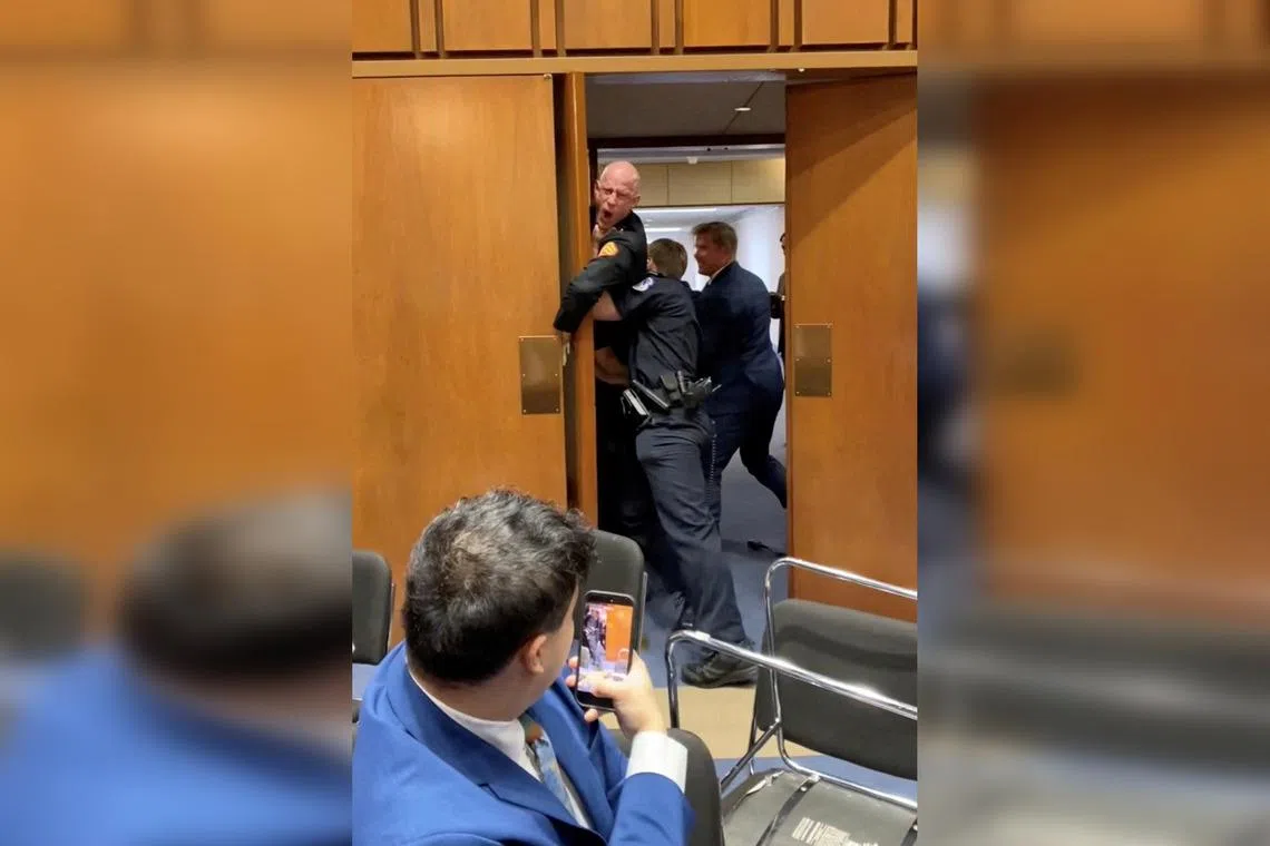 A video showed former Marine Brian McGinnis being dragged from the room by police officers and Republican Senator Tim Sheehy (right), before a sickening crack was heard due to his hand being trapped in the door.