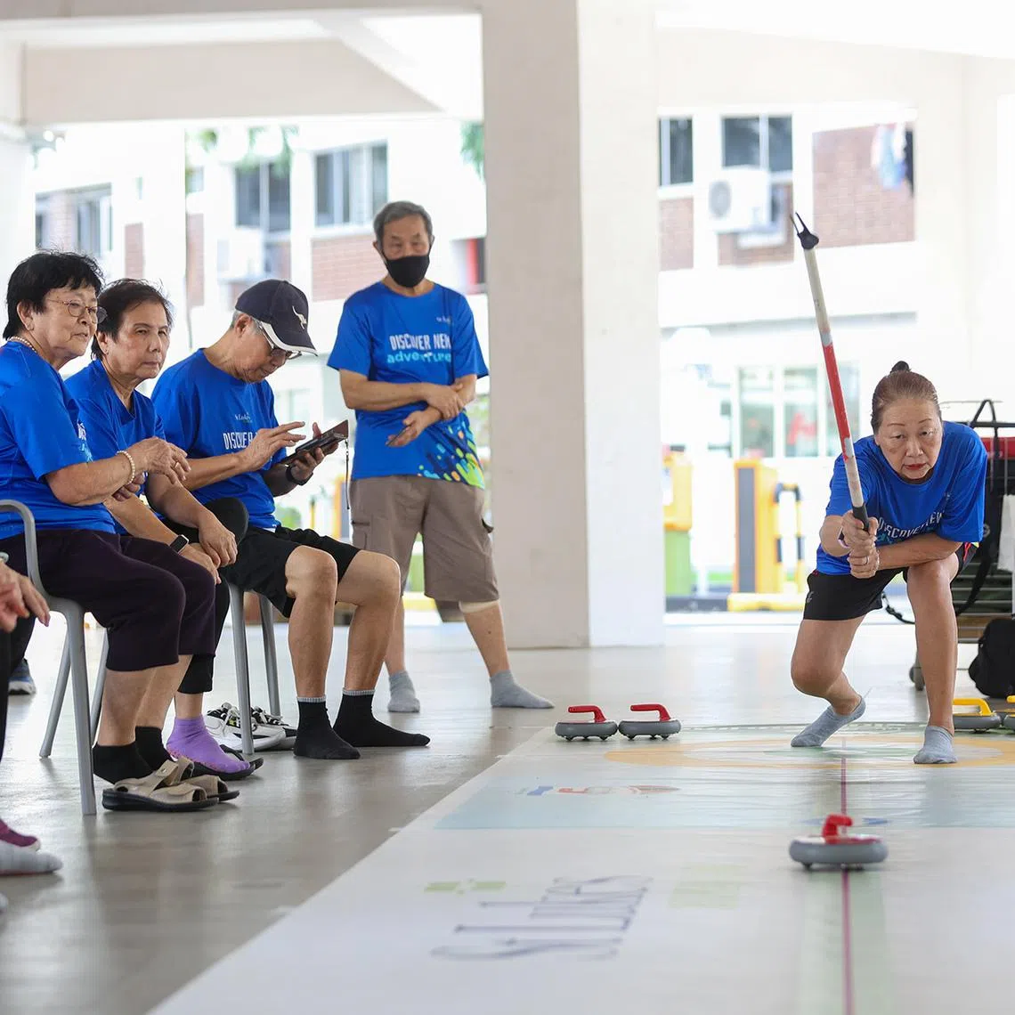 ST20260427_202651600842/Jasel Poh/jpcurling Retiree Agnes Chong follows through after releasing a rock during a game of floor curling at St Luke's ElderCare Active Ageing Centre (Care) @ Golden Years in Hougang on April 27, 2026. The 68-year-old has been playing the sport since May 2024 at the centre, where weekly sessions are held every Monday morning for two hours. The low impact variation of the winter sport helps keep seniors active mentally, requiring players to strategise the angle and strength of the release.
