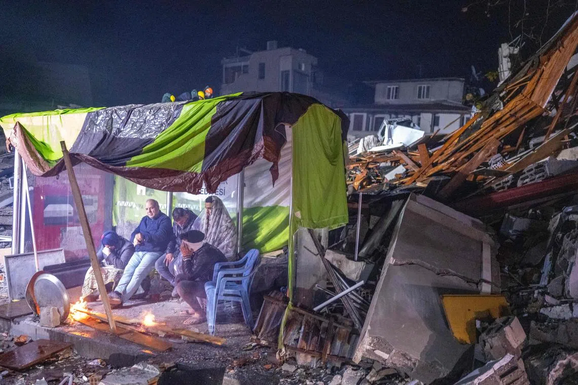 People take rest next to bonfire in the rubble in Hatay, Turkey, after a 7.8-magnitude earthquake struck the country's southeast on Feb 6, 2023.