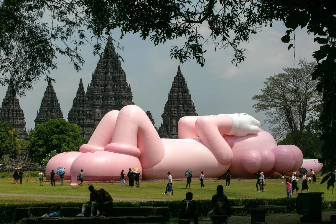 People looking at an art installation created by American artist Brian Donnelly, also known as Kaws, at the Prambanan Temple, one of the largest Hindu temples in Southeast Asia and a UNESCO World Heritage, in Yogyakarta on August 19, 2023.