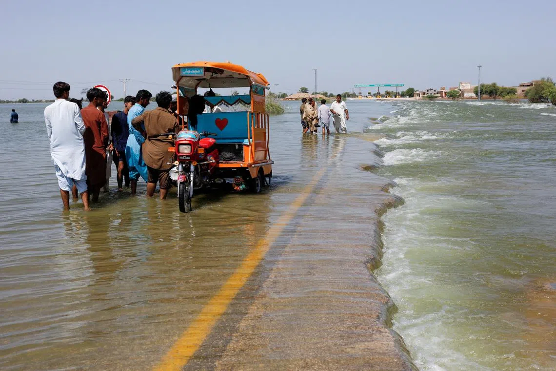 Displaced people stand on flooded highway, following rains and floods during the monsoon season in Pakistan, on Sept 16, 2022. 