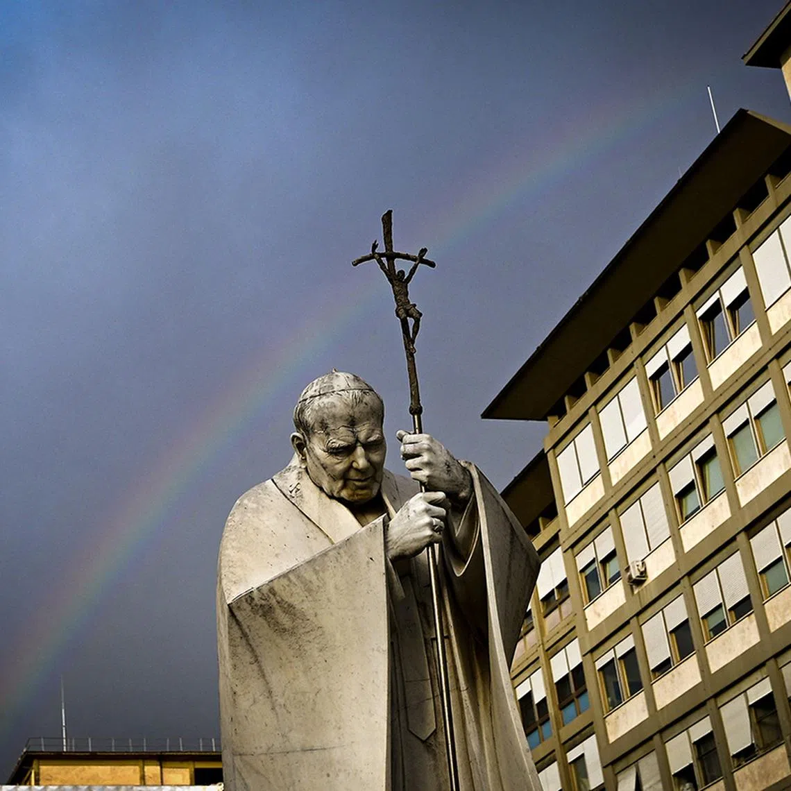 TOPSHOT - A rainbow appears above a statue of Pope John Paul II outside the Gemelli hospital where Pope Francis is hospitalised for tests and treatment for bronchitis in Rome, on February 18, 2025. The Vatican on February 18, 2025 cancelled two of Pope Francis's events at the weekend as the 88-year-old continues to receive hospital treatment for bronchitis. (Photo by Tiziana FABI / AFP)