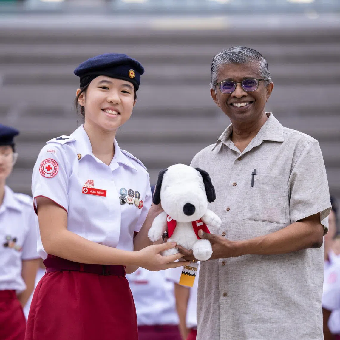ST20250415_202573400574/JKCPR20/Brian Teo/Joakim Kang/(From left) Alva Wong, 16, a secondary four student at Raffles Girls' School, receiving a Snoopy plush dressed in a Singapore Red Cross vest from Mr Benjamin William, secretary general and CEO of the Singapore Red Cross, during morning assembly at the school campus on April 15, 2025. Alva was recognised for performing CPR on a tourist suffering from cardiac arrest, helping to save their life before SCDF personnel arrived. ST PHOTO: BRIAN TEO 