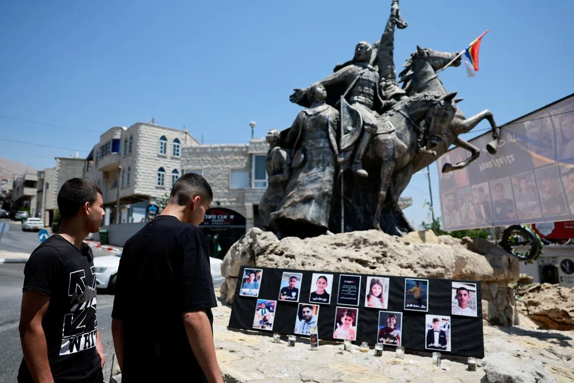Young people look at the pictures of children and teens killed at a soccer pitch by a rocket Israel says was fired from Lebanon, at a roundabout in Majdal Shams, a Druze village in the Israeli-occupied Golan Heights, July 29, 2024. REUTERS/Ammar Awad