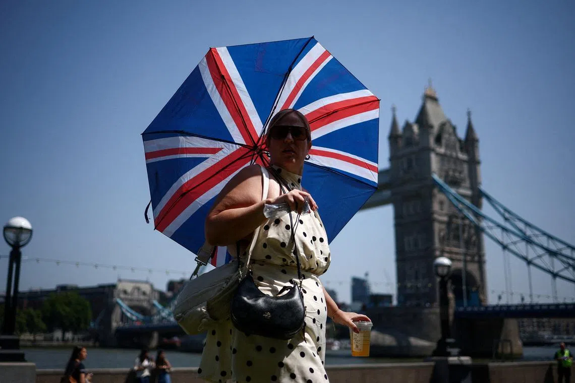 A woman uses an umbrella to shield herself from the sun while walking near Tower Bridge as Britain experiences record temperatures disrupting schools and transport networks, in London, Britain, June 25, 2026. REUTERS/Guglielmo Mangiapane