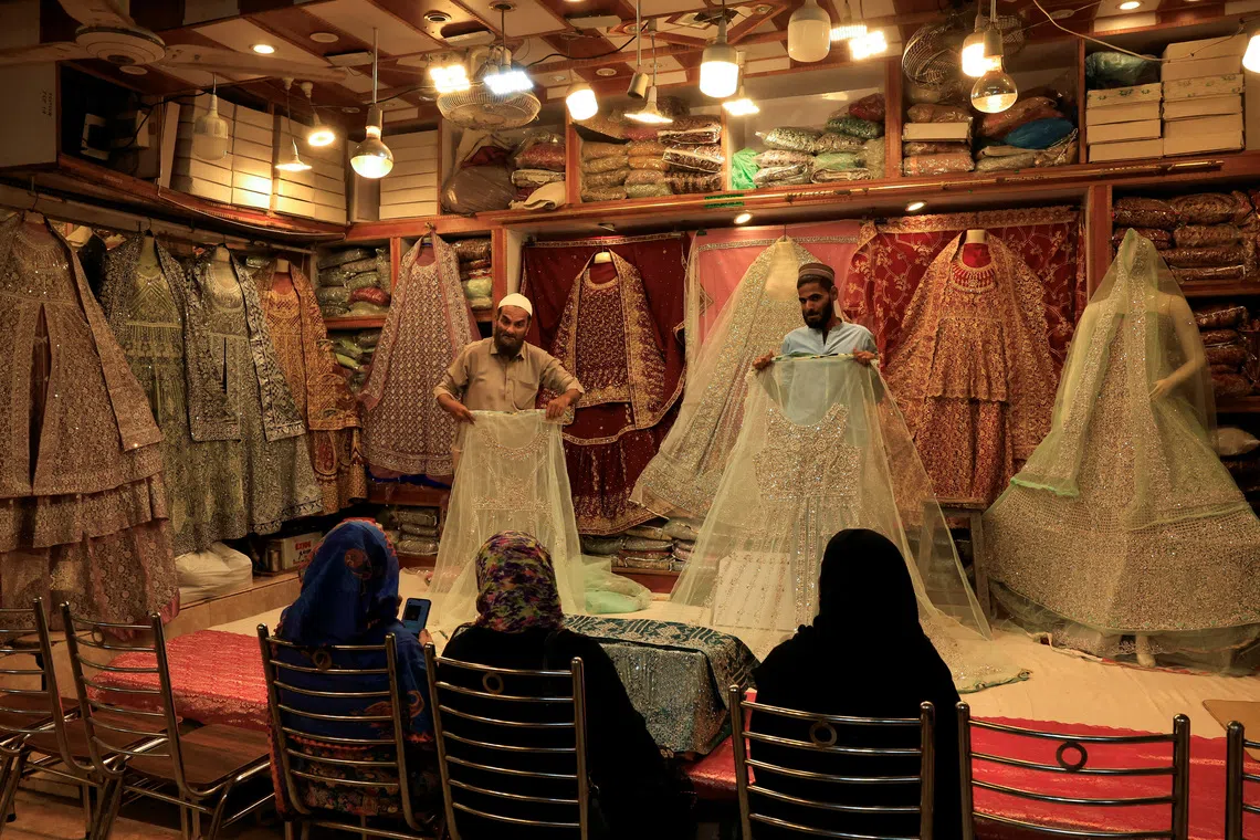 FILE PHOTO: Shopkeepers display bridal dresses to customers at a shop in a cloth market in Karachi, Pakistan September 23, 2025. REUTERS/Akhtar Soomro/File Photo