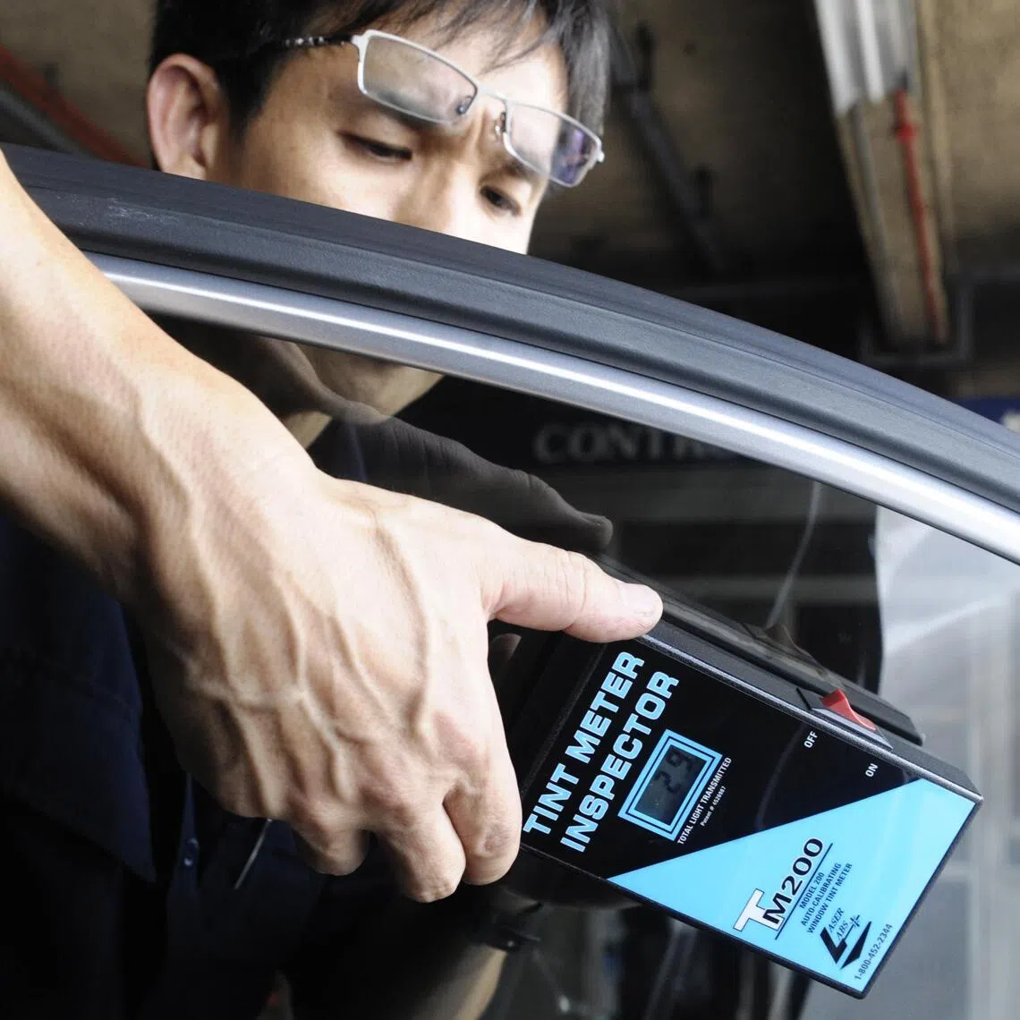 A vehicle inspector using a tint meter to measure the amount of light passing through a car window.