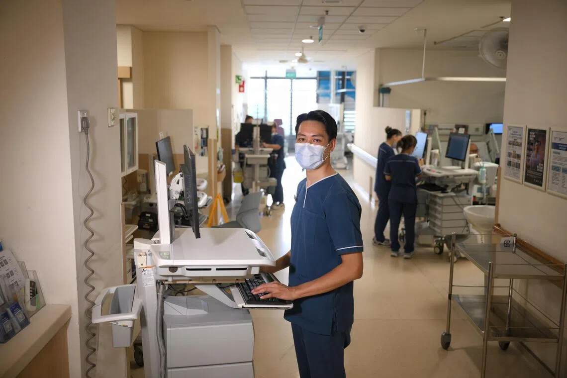 Former flight steward and army combat medic Tan Min Kai, now a staff nurse, updating patient records on a computer on wheels in the ward at Khoo Teck Puat Hospital.