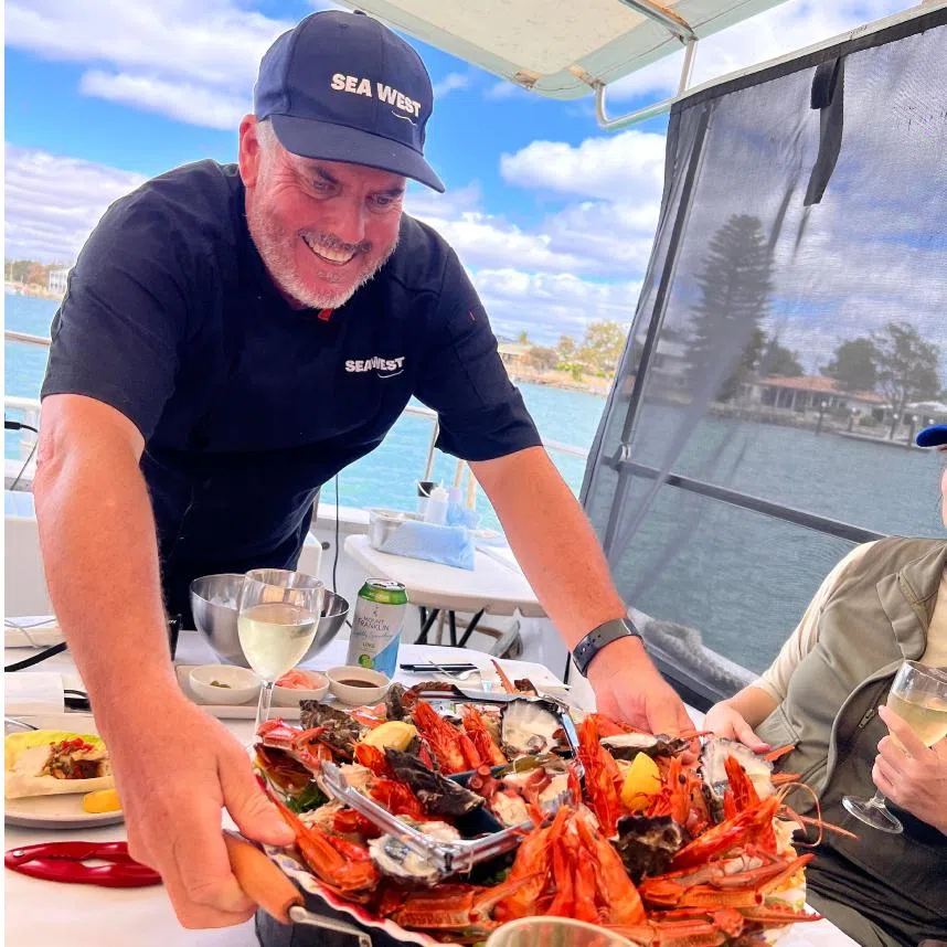 The Wild Seafood Experience by Mandurah Cruises is a three-and-a-half-hour tour that includes a seven-course seafood spread and catching your own wild lobsters for lunch, which the writer posing with.