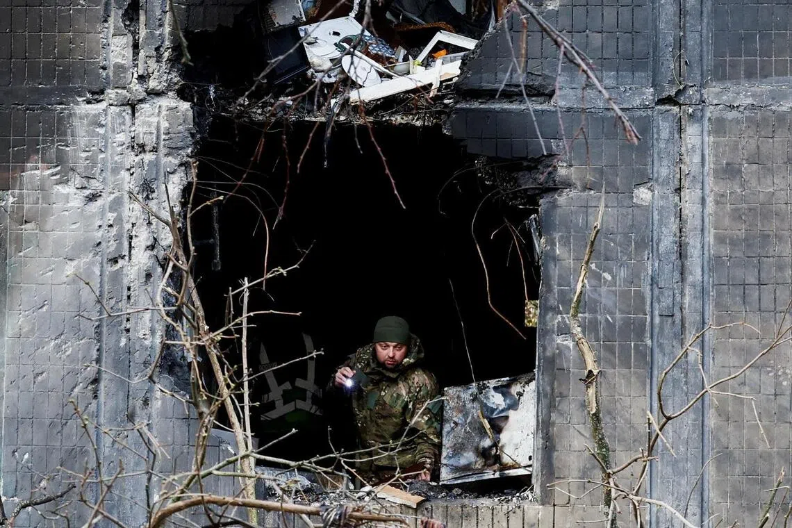 An investigator looking through the window of an apartment building damaged during an overnight Russian drone and missile strike, in Kyiv, on Nov 14.