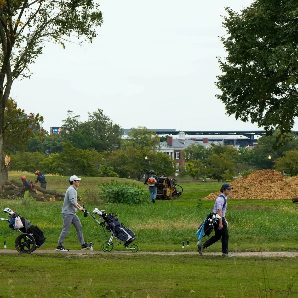 Golfers walk past workers removing trees at East Potomac Golf Links golf course in Washington, DC, on Oct 10.