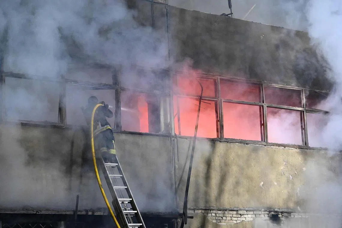 Firefighters equipped with fire hoses try to put out a fire at a civilian industrial enterprise following a drone attack in Kharkiv on April 2, 2025, amid the Russian invasion of Ukraine. (Photo by SERGEY BOBOK / AFP)