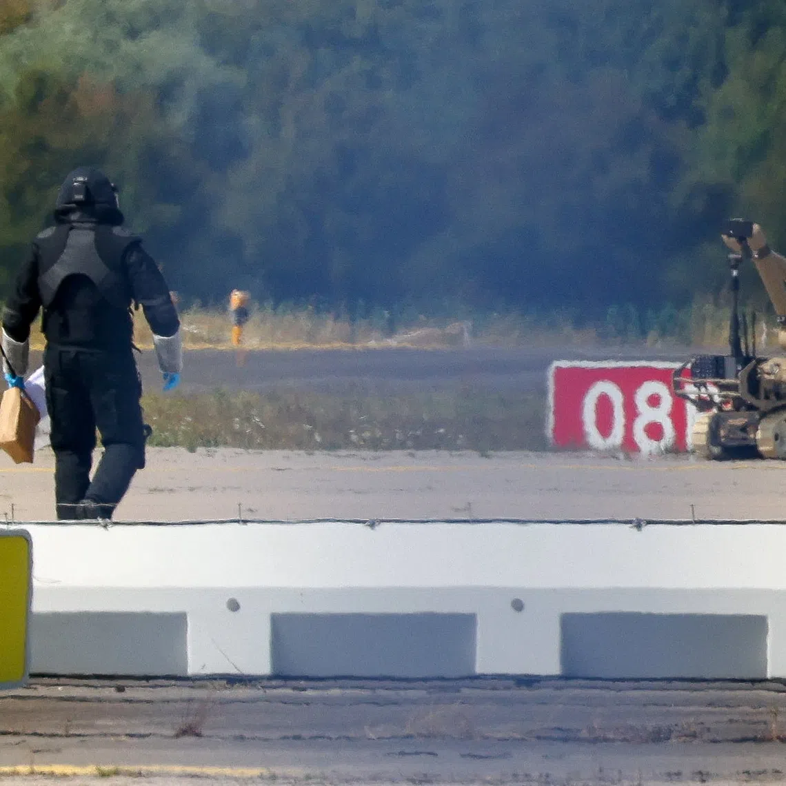 A police officer in protective clothing walks next to an explosive-disarming robot (EOD) at Leipzig/Halle Airport in Schkeuditz, Germany, August 5, 2026, after the police said explosives experts examined a drone found near a runway, and after a DHL cargo aircraft hit an unknown object as it was climbing away from the airport overnight, prompting an unscheduled landing in Hanover, according to a source familiar with the incident. REUTERS/Axel Schmidt