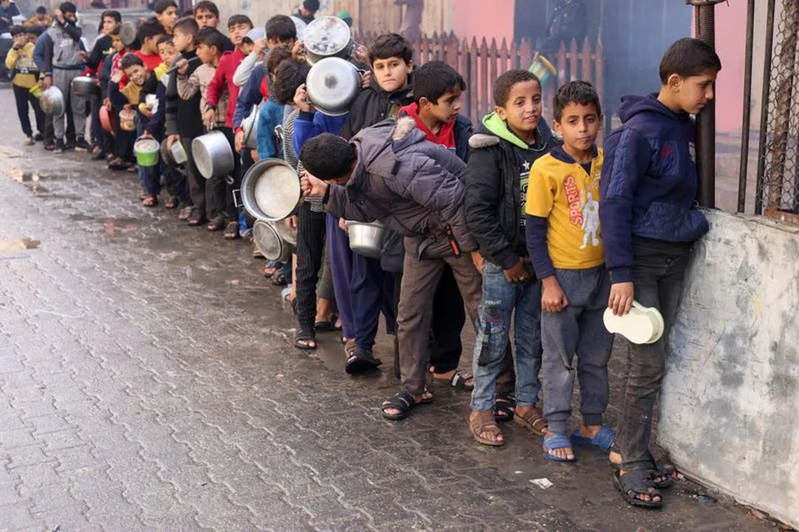 Palestinian children carry pots as they queue to receive food cooked by a charity kitchen, amid shortages in food supplies, as the conflict between Israel and Hamas continues, in Rafah in the southern Gaza Strip December 14, 2023. REUTERS/Saleh Salem/File Photo