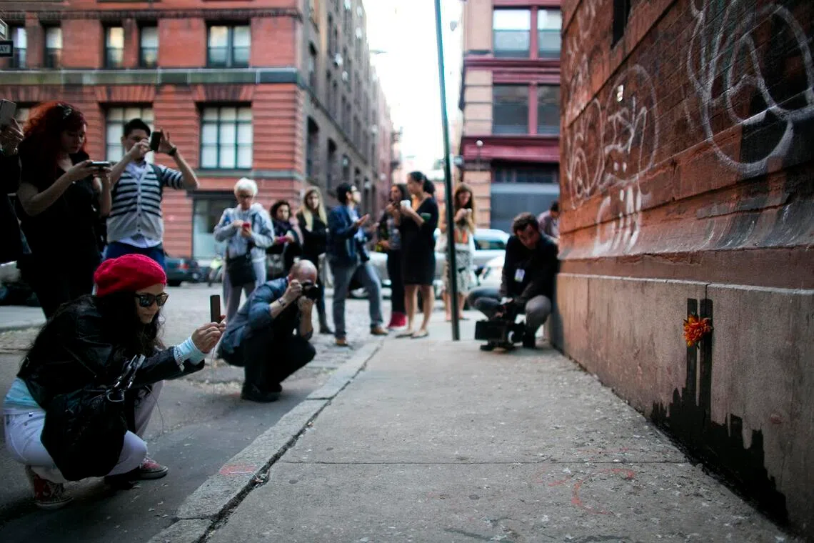 People taking photos of a piece of art by Banksy on a wall in New York on Oct 15, 2013.