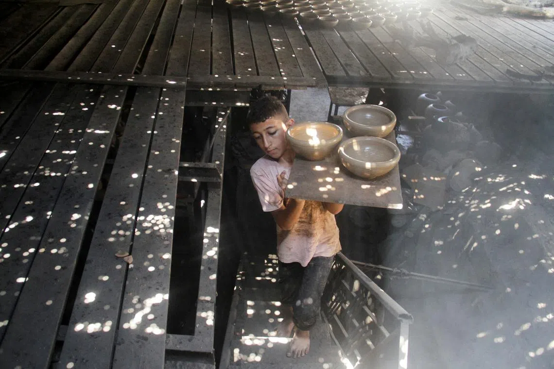 FILE PHOTO: A boy carries pots as Palestinians work in a pottery workshop to respond to an increase in the demand for clay pots used to cool water due to power cuts and hot weather, according to workers, amid the Israel-Hamas conflict, in Gaza City August 13, 2024. REUTERS/Mahmoud Issa/File Photo