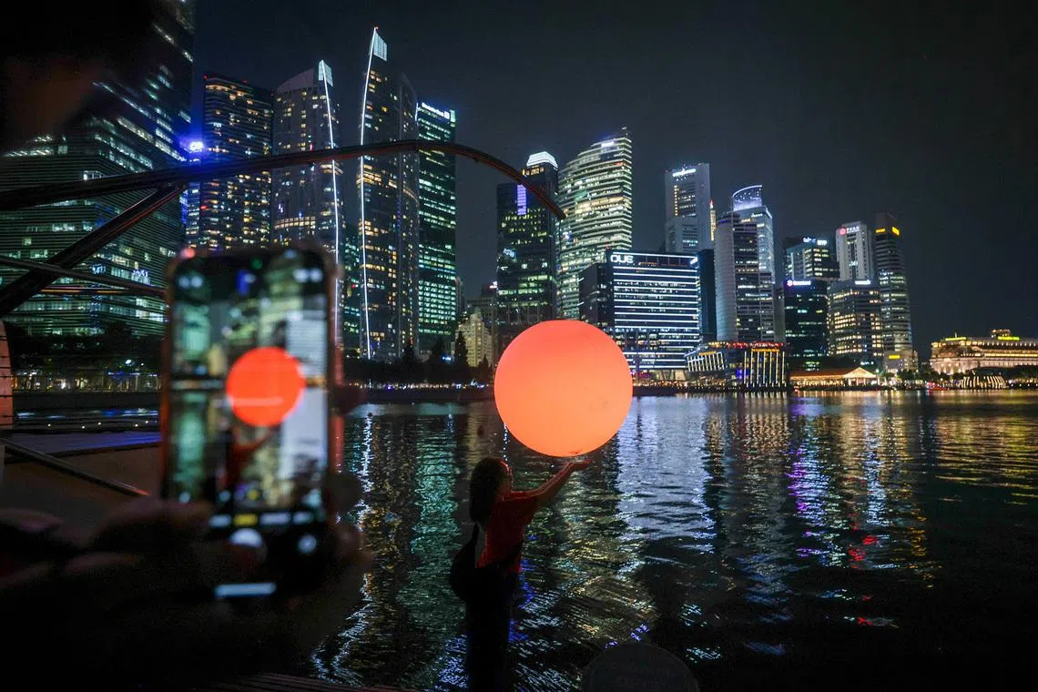 iLight Singapore 2026 media preview - Passers-by experiencing an installation by Chinese artist Wentao Wang called “Let’s Fish The Sun”, at the Marina Bay Lower Boardwalk, on June 3, 2026. The piece involves a fishing rod extending over the water, suspending a luminous orb hovering just above the surface. It is one of a series of installations for i Light Singapore, which opens on June 5. 